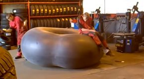 Man Sits On An Overinflated Tyre Tube, And Another Man Pops It