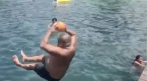 Man throws a ball high up in the air while diving in the pool